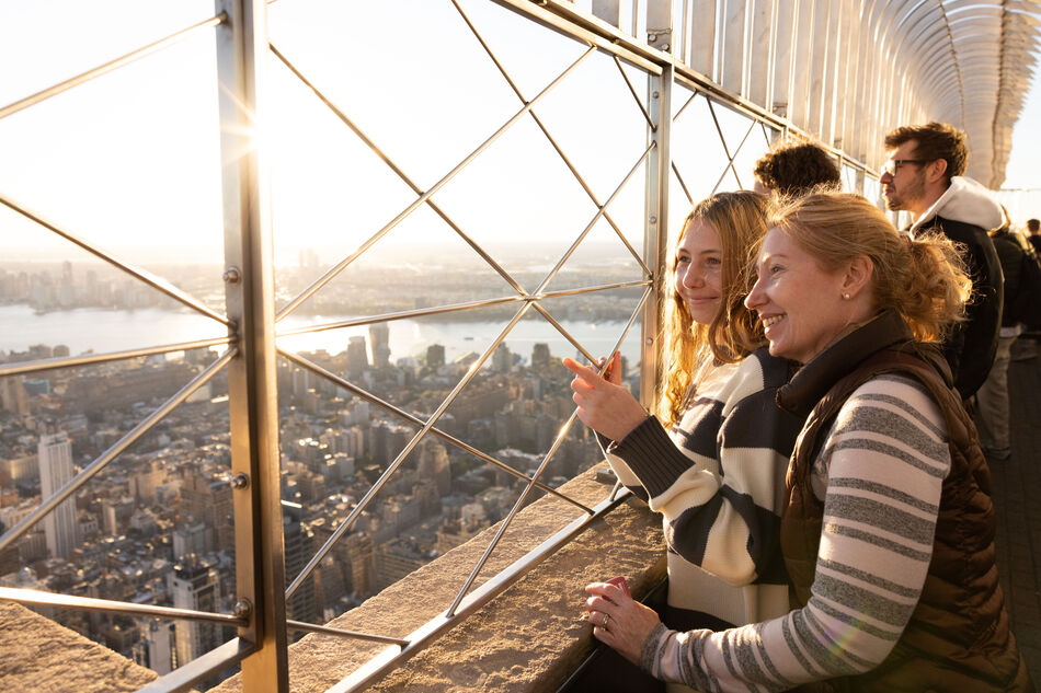 People looking out at NYC from the 86th floor observation deck at the Empire State Building Observatory.