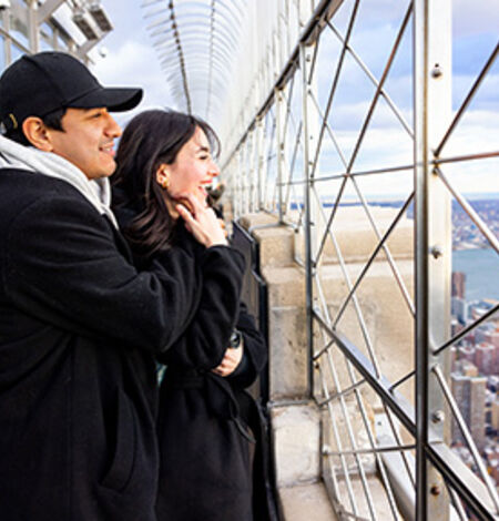 People looking out at NYC from the 86th floor observation deck at the Empire State Building Observatory.
