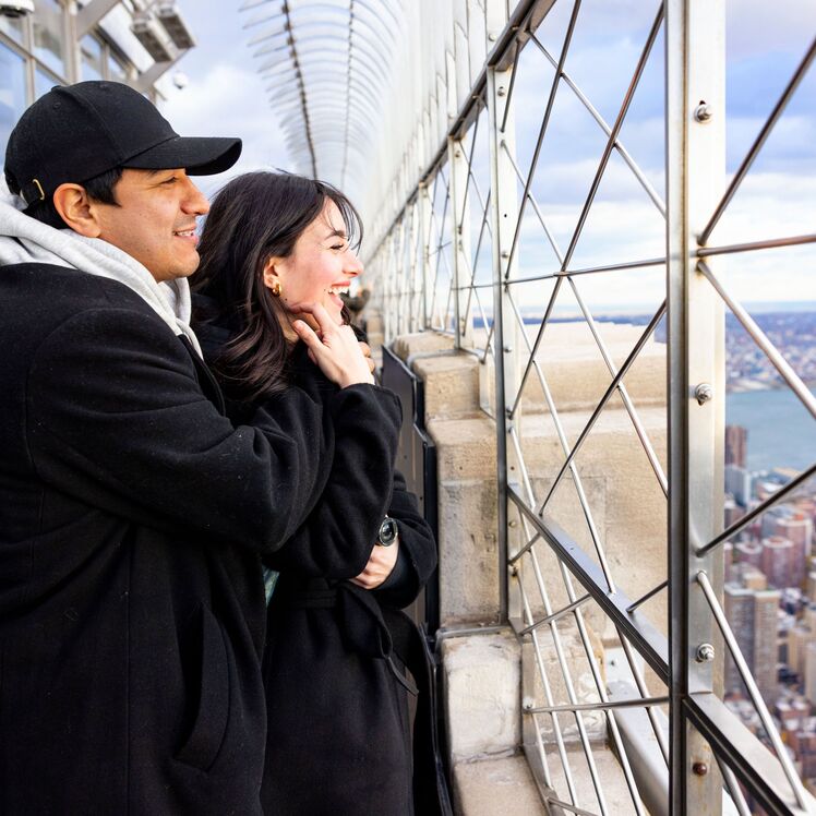 People looking out at NYC from the 86th floor observation deck at the Empire State Building Observatory.