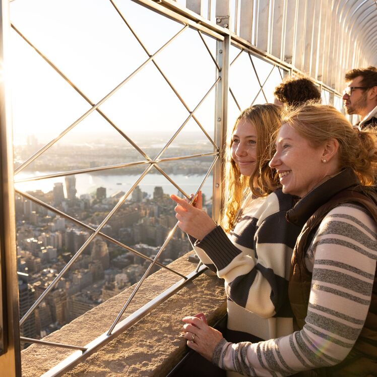 People looking out at NYC from the 86th floor observation deck at the Empire State Building Observatory.